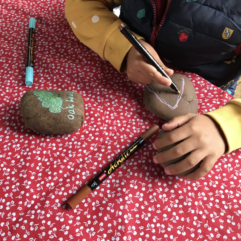 A photo of a child's hands painting leaves on rocks