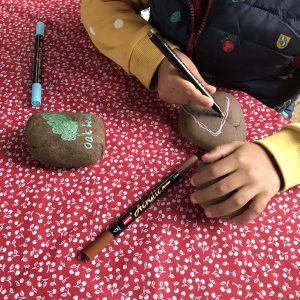 A photo of a child's hands painting leaves on rocks