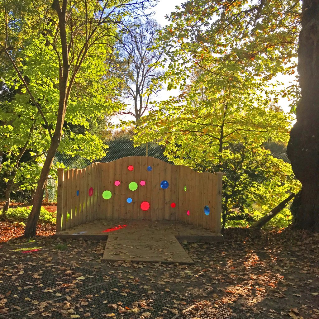 A photo of a wooden platform surrounded by coloured perspex portholes amidst autumn trees